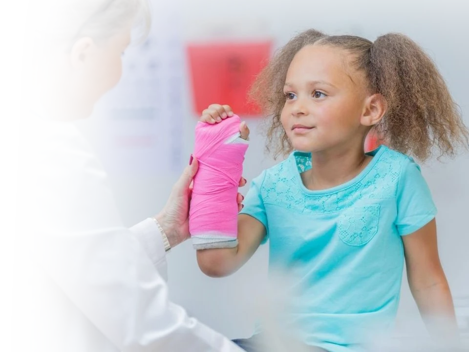 A doctor holding a girls wrist with a cast on it.